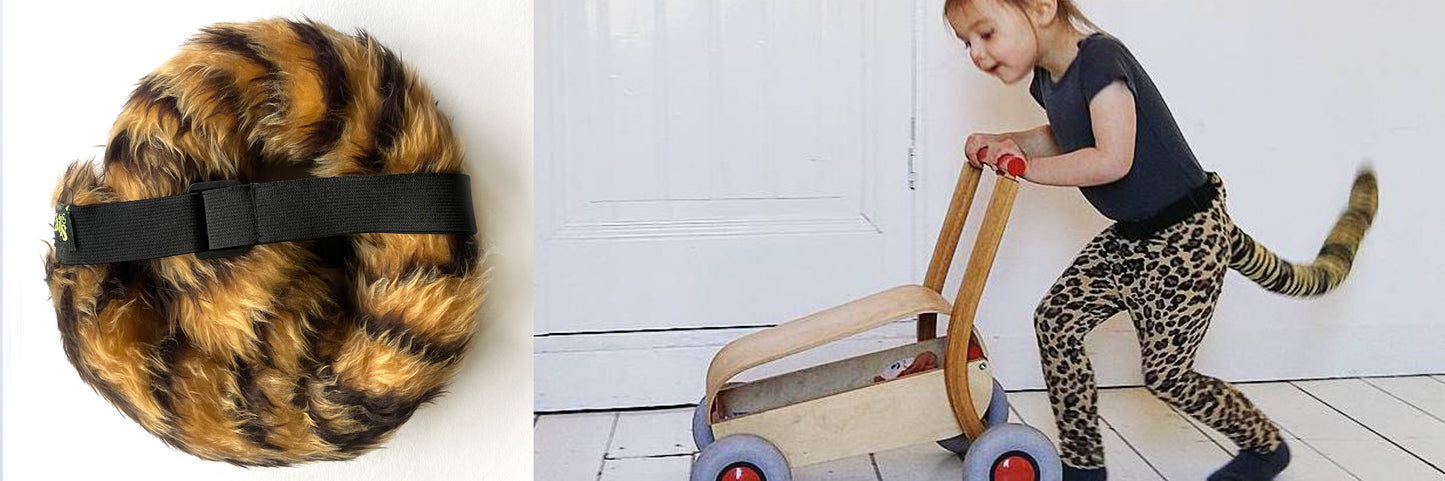 A child in leopard print pants and a matching tail from TellTails The Tiger collection pushes a wooden toy cart. The furry, tiger-striped belt complements the outfit, perfect for whimsical festivals or fancy dress occasions.