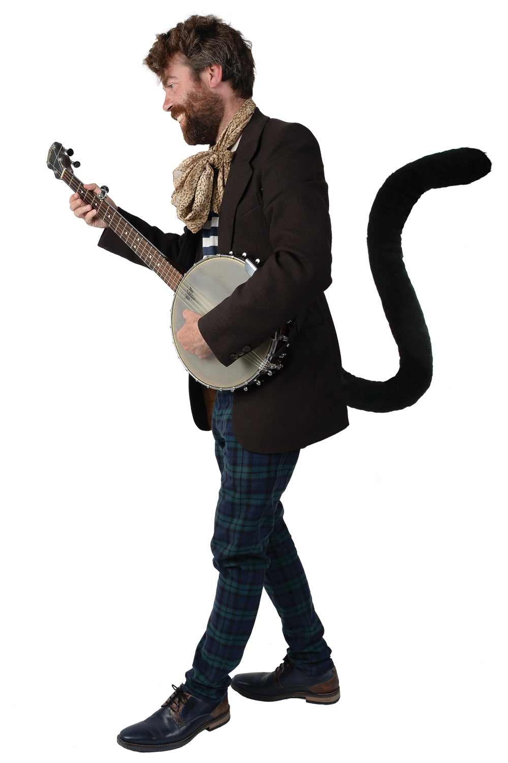 A man in a festive ensemble stands against a white backdrop, donning a brown blazer, patterned scarf, green plaid pants, and blue shoes. A TellTails Black Cat tail accessory playfully enhances his outfit as he smiles in profile.